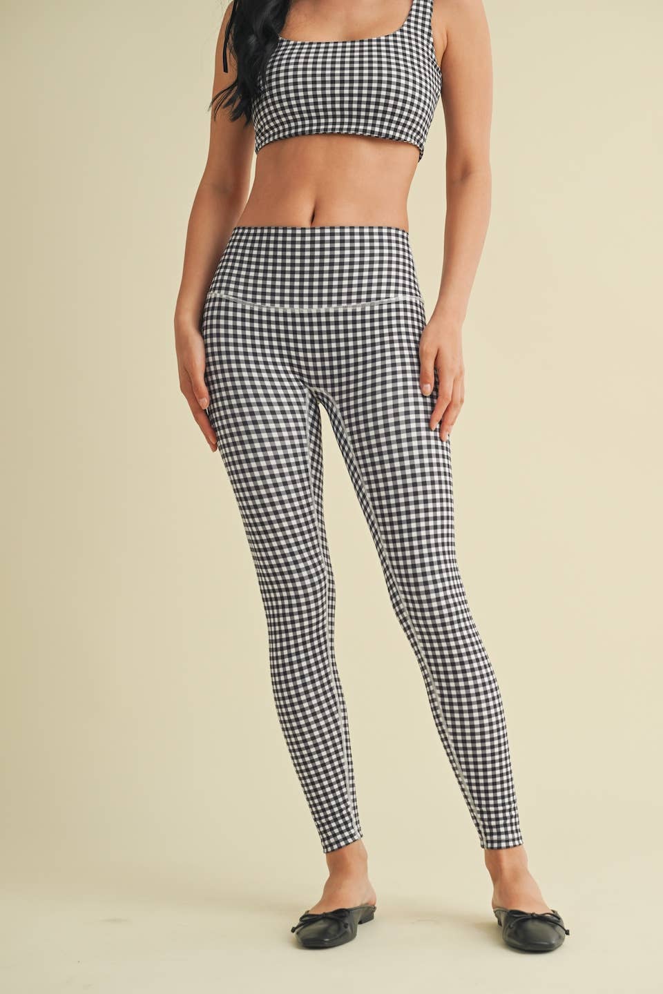 Person wearing a black and white checkered top and leggings on a beige background